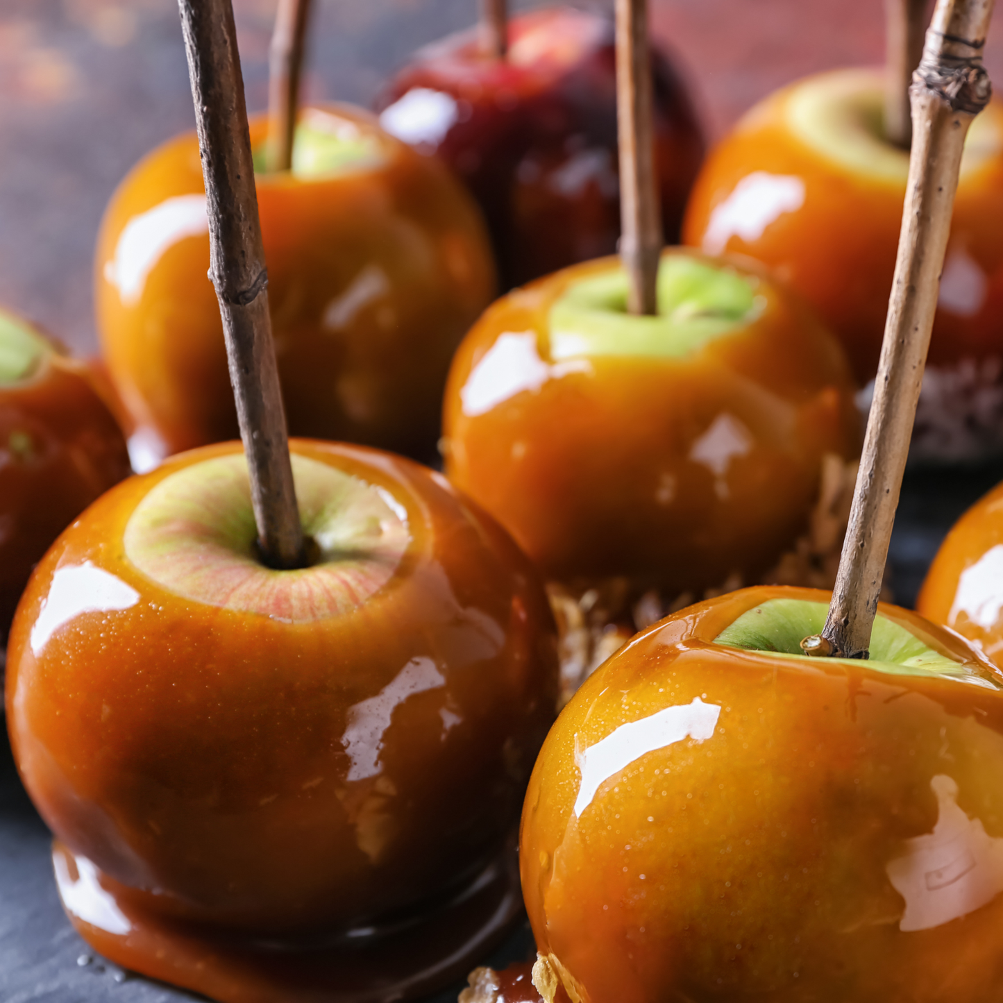 Close-up of glossy caramel apples on sticks set against a dark background.