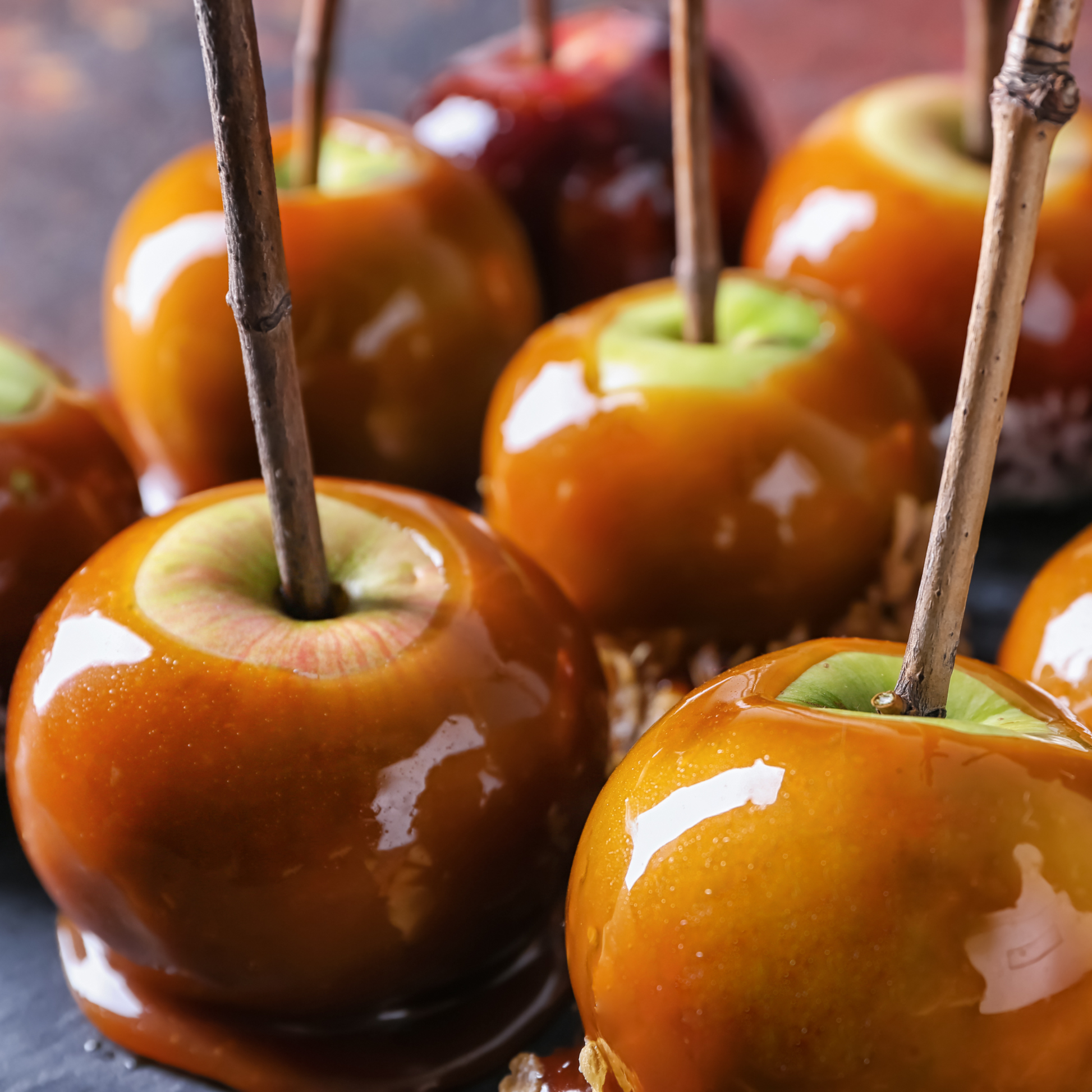 Close-up of glossy caramel apples on sticks set against a dark background.