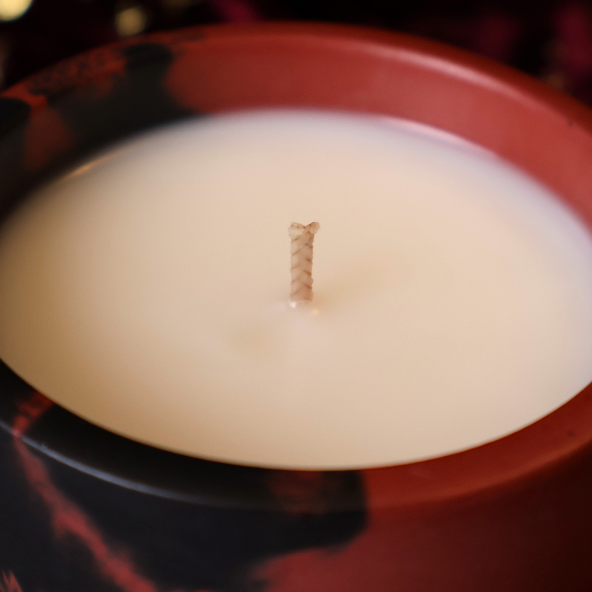 A close-up shot of a white wax candle in a dark red and black marbled hydrostone container, featuring a single braided wick in the center.