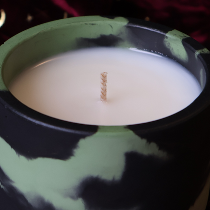 A close-up of a candle in a black and light green marbled hydrostone container, filled with white wax and featuring a single wick.